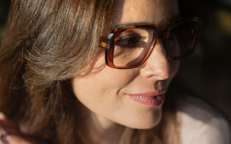 Nahaufnahme einer lächelnden Frau mit braun gemusterter Korrektionsbrille genießt natürliches Licht und scharfes Sehen.