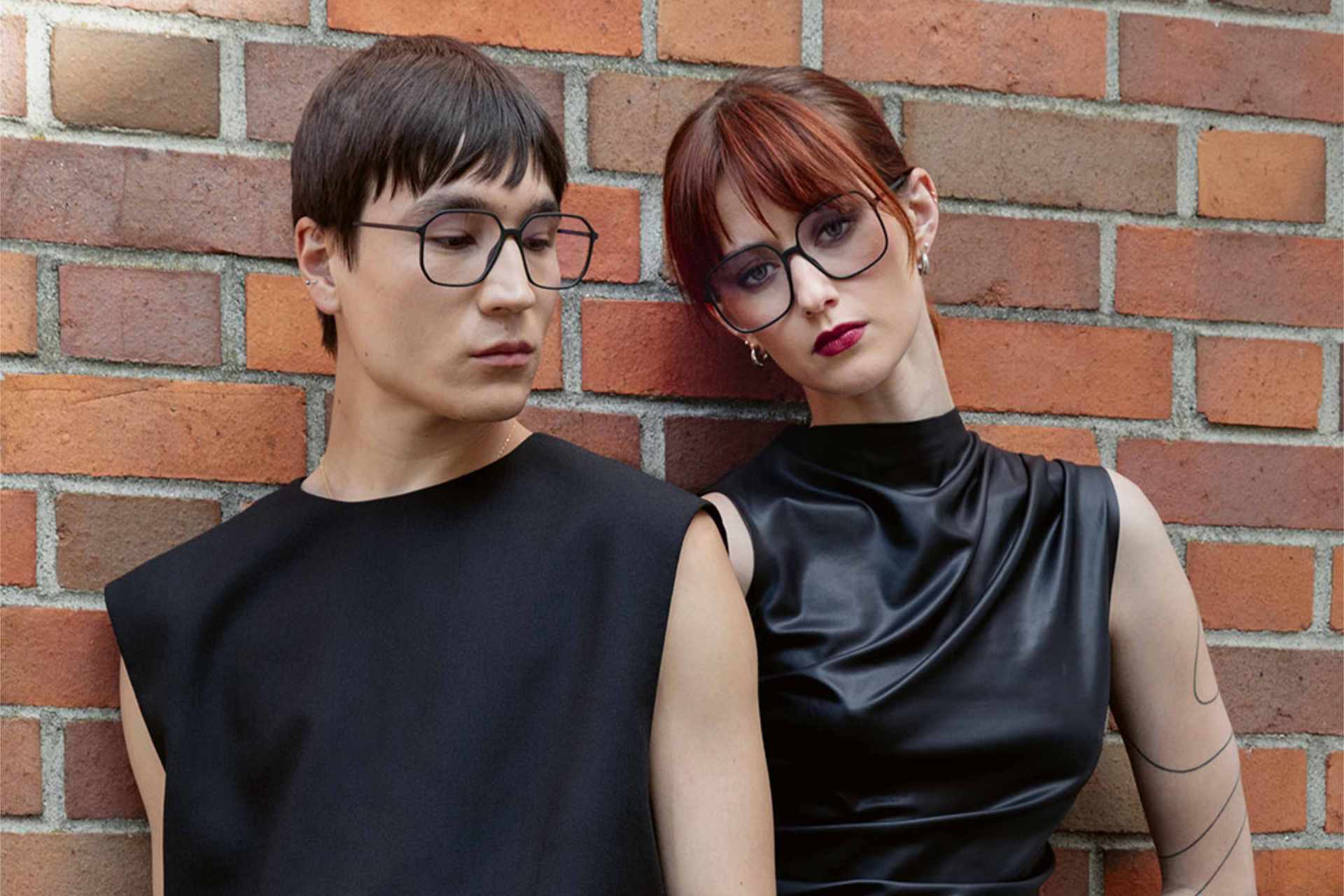 Zwei Frauen stehen vor einer Klinkerwand und tragen Brillen von NEUBAU.